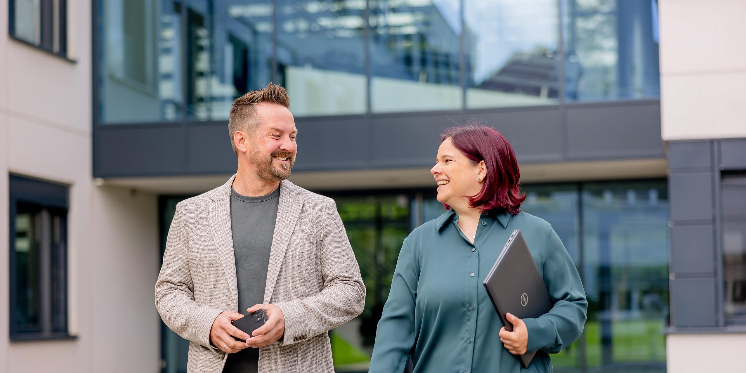 Ein lächelnder Mann und eine Frau vor einem Firmengebäude von VOSS.