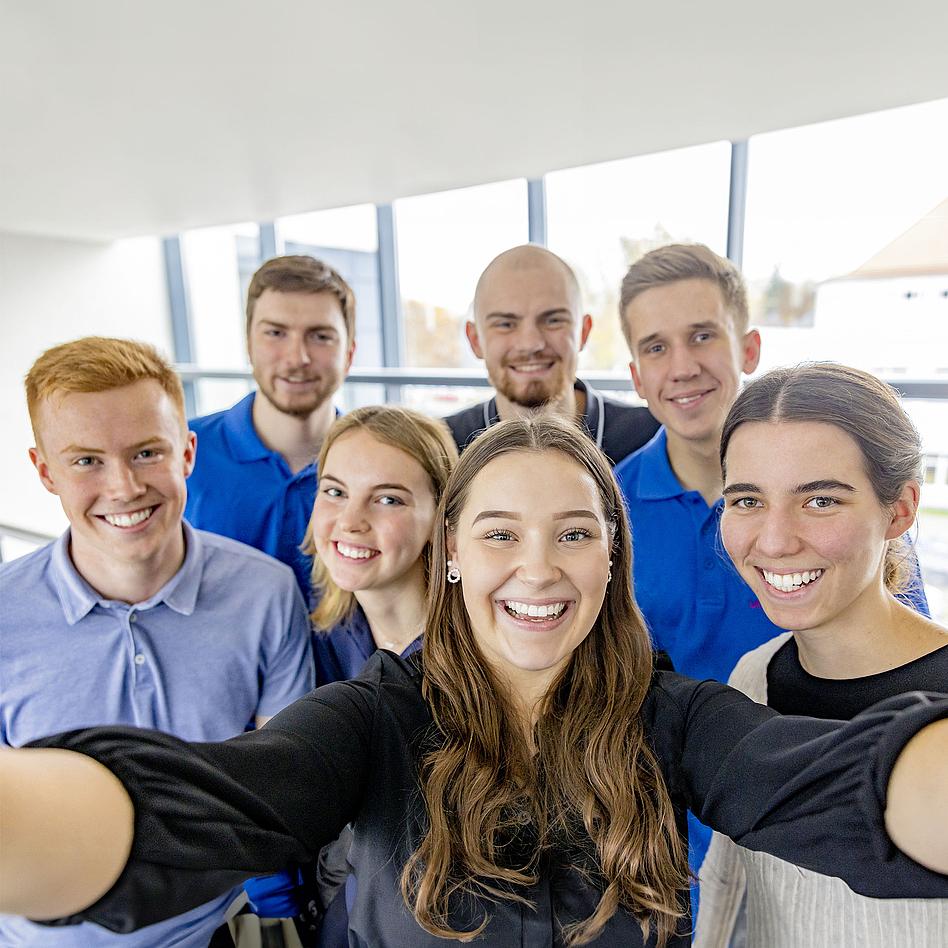 Eine Gruppe junger, lächelnder Menschen machen ein Selfie.