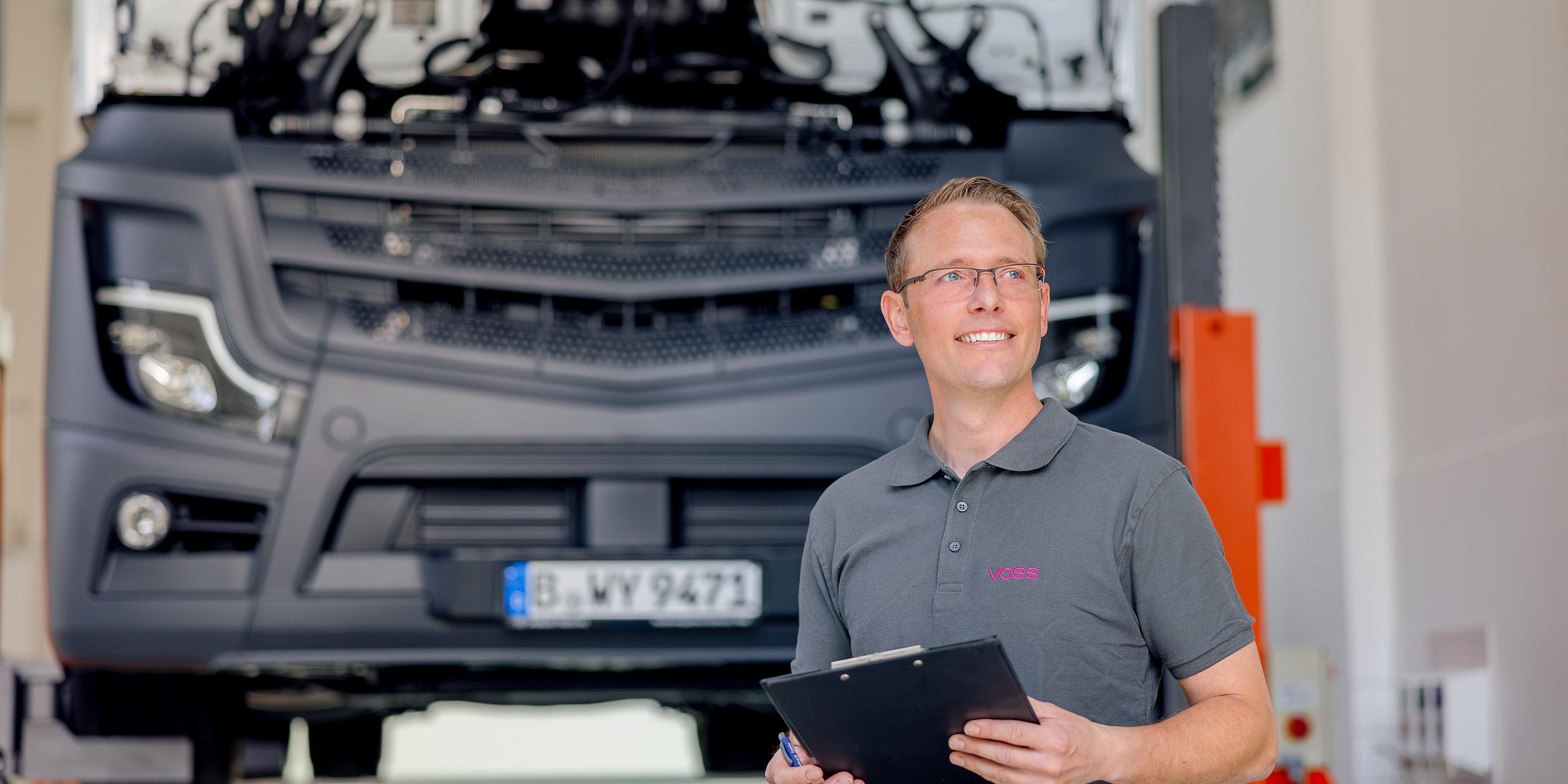 VOSS Mitarbeiter mit Klemmbrett in der Hand steht vor einem Lkw. 