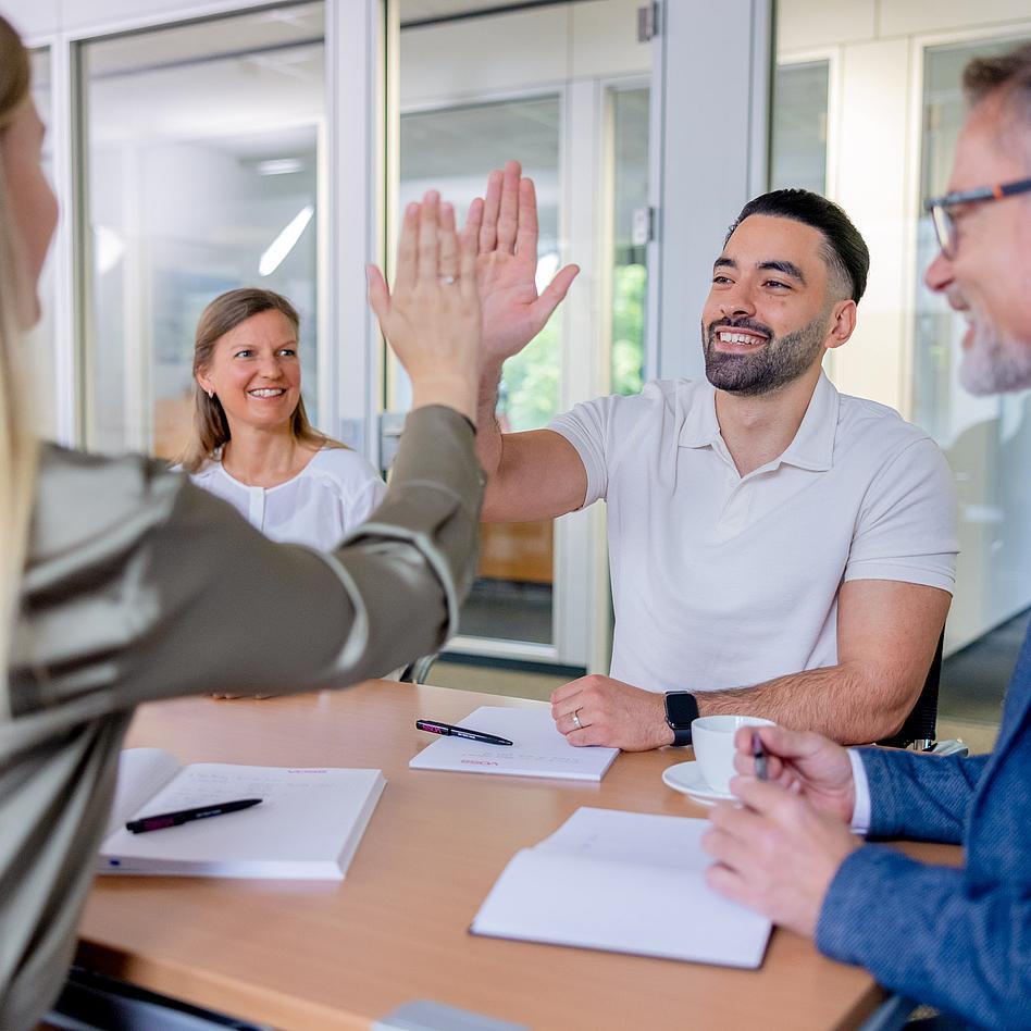 Vier Personen sitzen an einem Tisch, zwei Personen machen High Five.