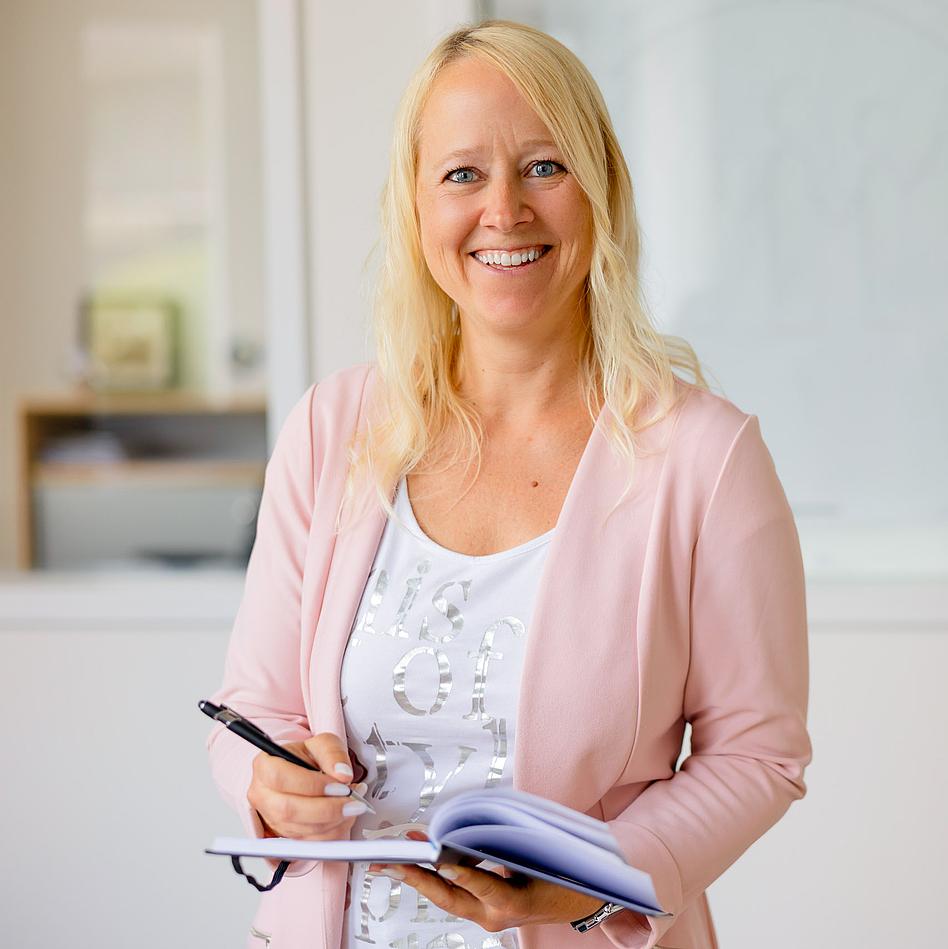 Eine blonde Frau mit einem Terminplaner und einem Stift in der Hand.