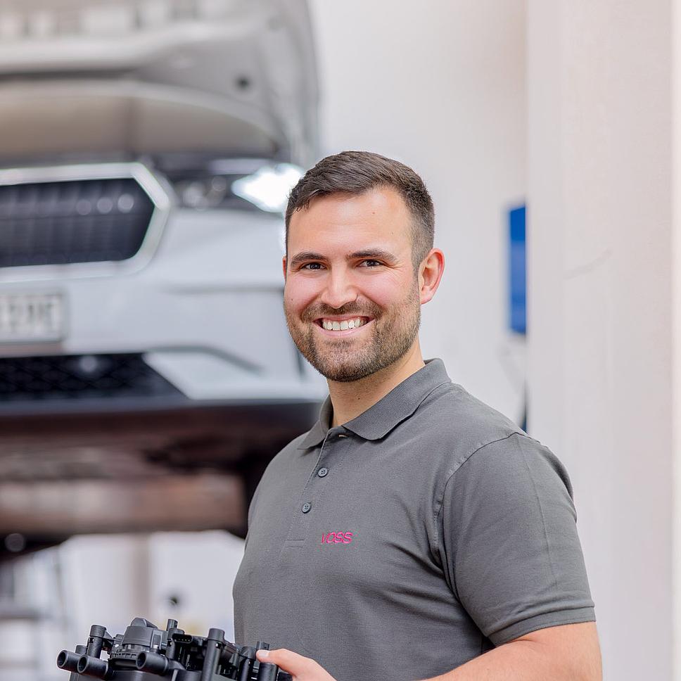 Mann mit Bauteil vor Auto in Fertigung