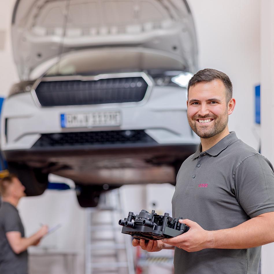 VOSS Produktionsmitarbeiter mit Bauteil vor Auto.