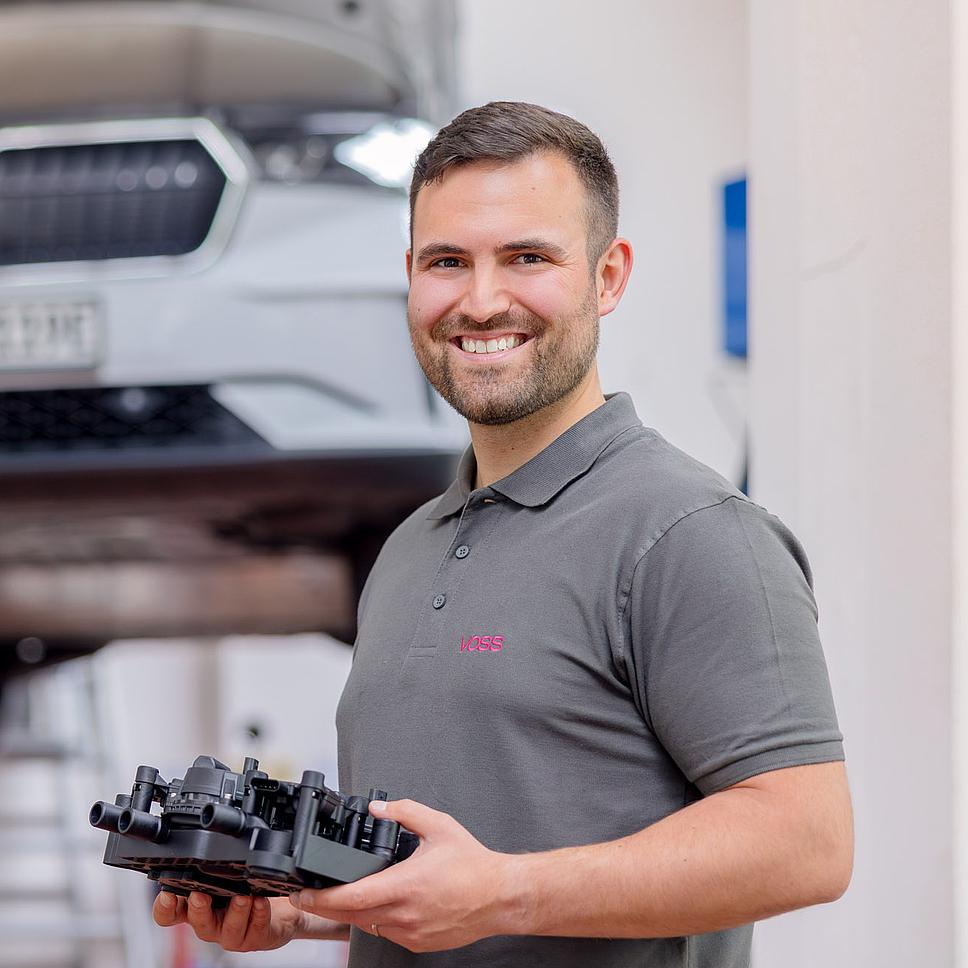 Mann mit Bauteil vor Auto in Fertigung