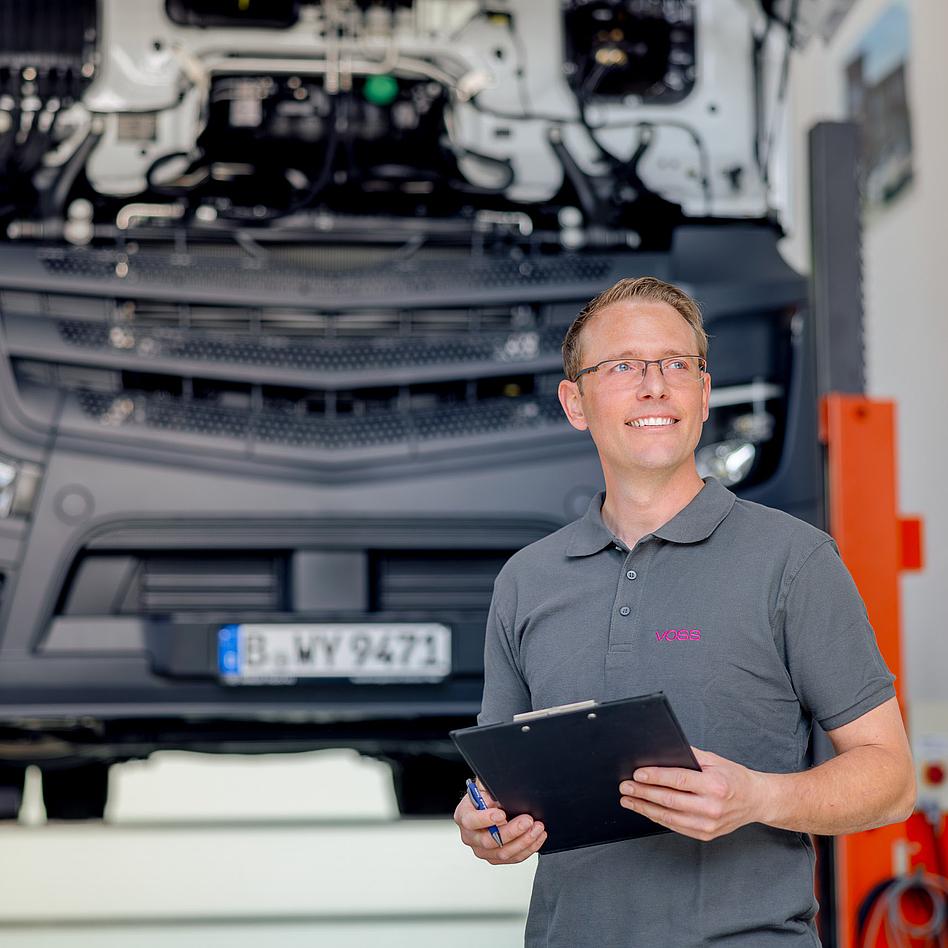 VOSS Mitarbeiter mit Klemmbrett vor Pkw mit geöffneter Motorhaube.