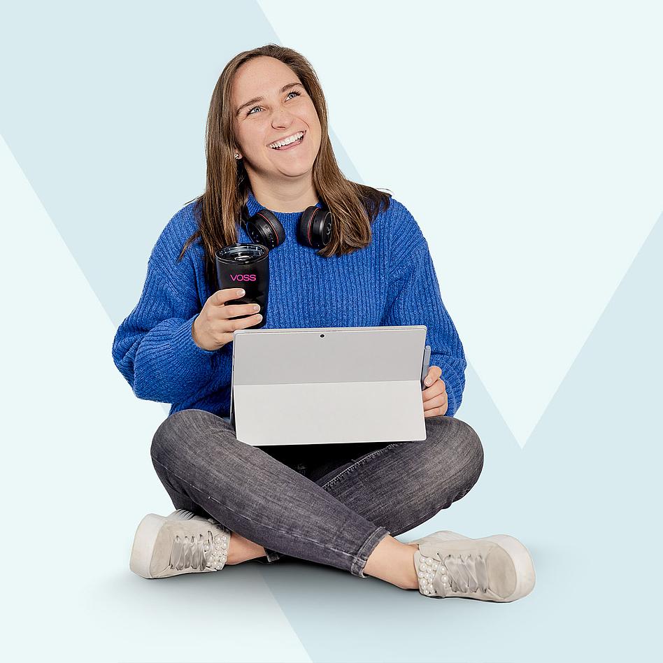 Junge Frau sitzt im Schneidersitz mit VOSS Becher und Surface in der Hand.