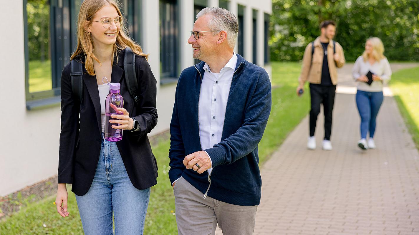 Zwei Personen laufen gefolgt von zwei weiteren auf einem Weg neben einem Gebäude.