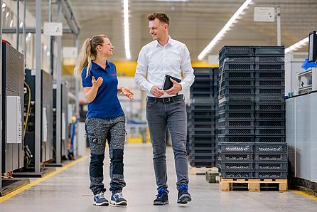 Büro und Produktionsmitarbeiter laufen durch die Produktion und unterhalten sich miteinander